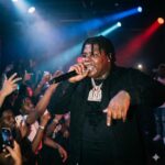 BigXthaPlug Rapper performing on stage with a microphone, energetic crowd and colorful stage lights behind him.