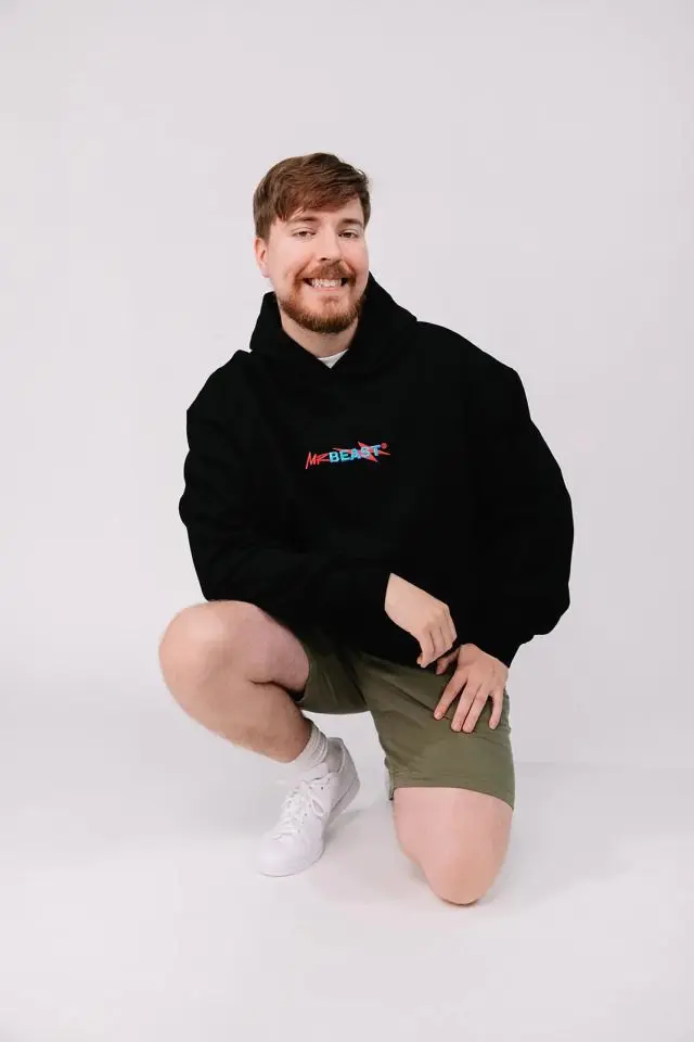 Jimmy Donaldson MrBeast crouching in a black MrBeast hoodie and shorts during a photo shoot